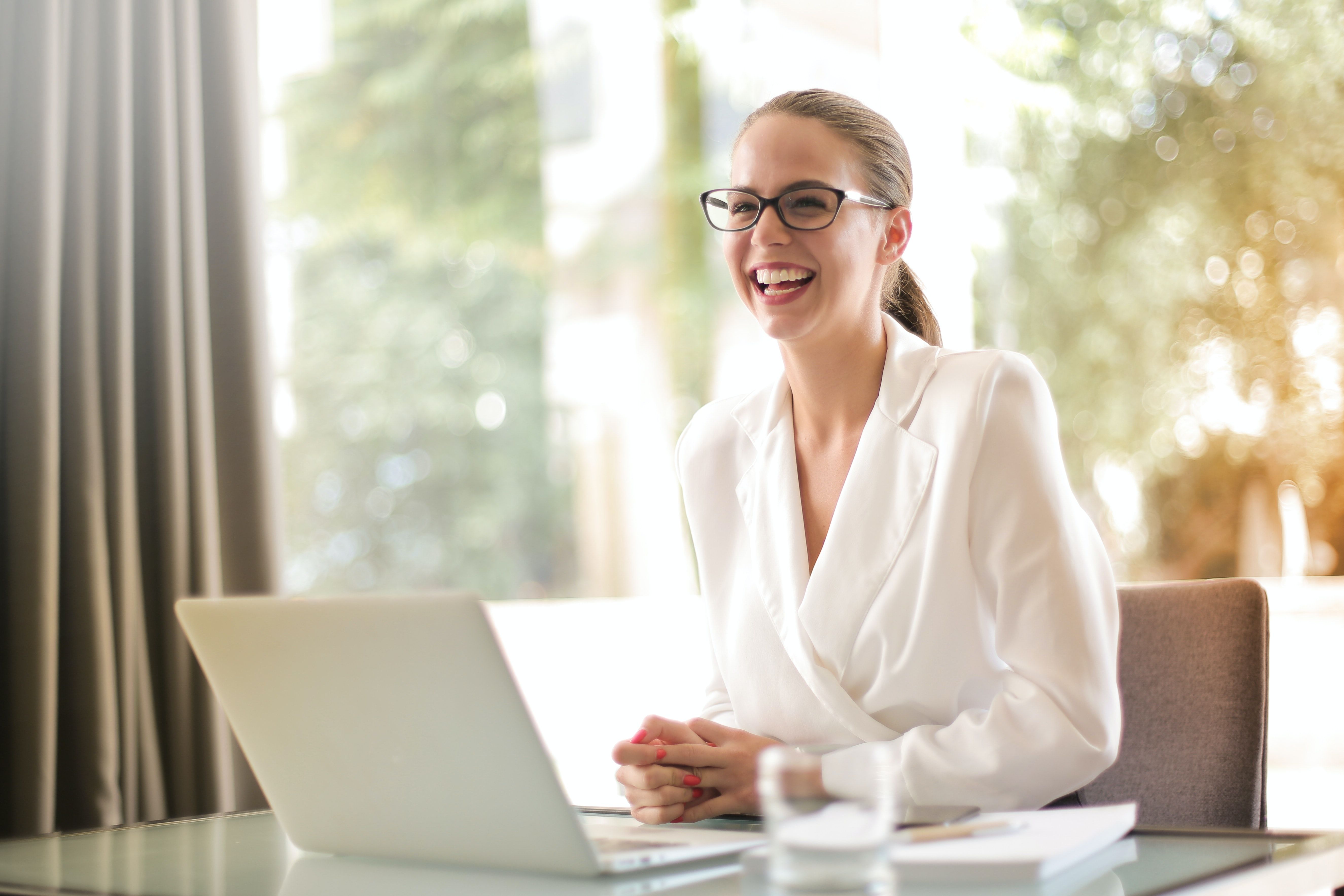 Woman wearing white shirt and glasses smiling in front of a computer